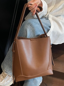 Brown leather bucket bag with pebble texture and wide strap shown in lifestyle setting