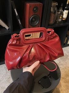 Minimalist red pleated tote bag with high-gloss finish on a black table