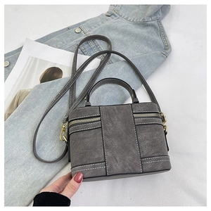 Detail der grauen Ledertasche mit weißen Kontrastnähten und goldfarbenen Metallbeschlägen