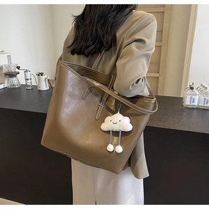 Brown leather tote bag featuring a cute white cloud plush pendant in a cafe setting