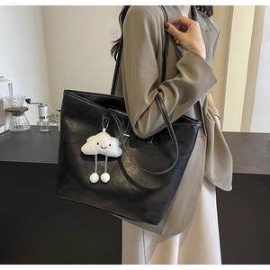 Close-up of black textured leather tote with contrast stitching and cloud plush charm
