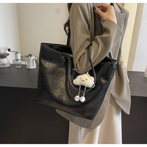 Shoulder view of black leather tote bag with white stitching and plush cloud charm