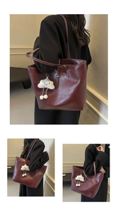 Detail view of large burgundy tote bag with a white plush charm and slim shoulder straps