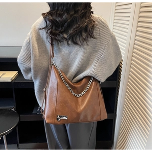Detail of a brown leather hobo bag with silver chain handle and heart charm detail