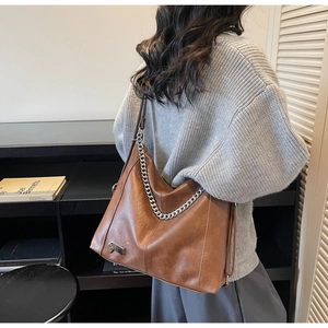 Detail of a brown vintage tote bag with a bold silver chain and shiny leather texture