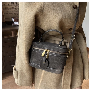 Makroaufnahme der dunkelgrauen Krokodilledertasche mit weißen Kontrastnähten und Goldzipper