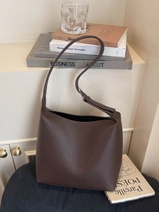 Minimalist dark brown lychee leather bucket bag with silver buckle in home setting