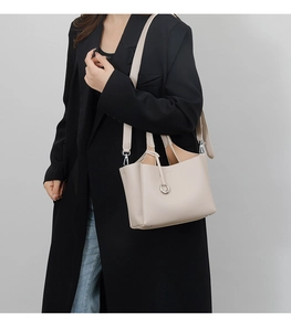Dettaglio della borsa tote in pelle color crema con grana litchi e anello in metallo su modella