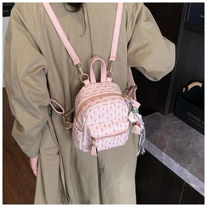 Close-up of a pink tweed mini backpack featuring a plush tassel charm on a model