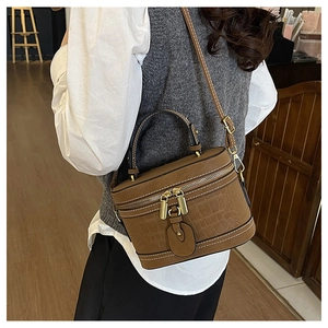 Detailansicht der dunkelbraunen Kroko-Zylindertasche mit Gold-Reißverschlüssen und Griff