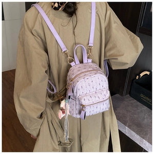 Close-up of a lavender tweed mini backpack with gold hardware worn on a trench coat