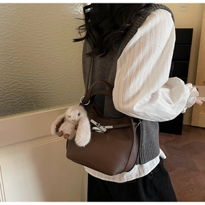 Detail of dark brown lychee leather handbag with silver lock and plush bunny charm
