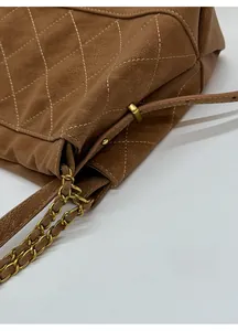 Detail of brown quilted leather texture and adjustable gold chain strap on shoulder bag
