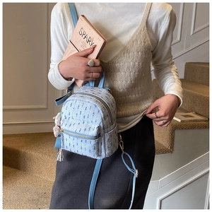 Close-up of light blue tweed backpack with golden zipper and fluffy pompom accessory