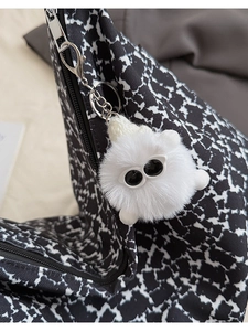 Close-up of white plush monster keychain with big eyes attached to a checkered bag