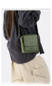On-body shot of a dark green textured leather crossbody flap bag with black strap