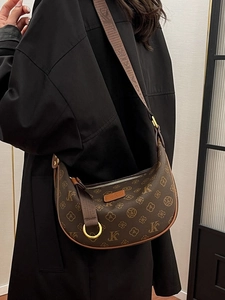 Chic brown monogram croissant bag with adjustable strap worn over a black trench coat