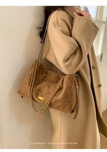 Close-up of brown suede quilted shoulder bag with gold chain strap on a model coat