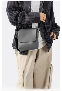 Detail of grey leather crossbody bag with brand logo and adjustable nylon strap