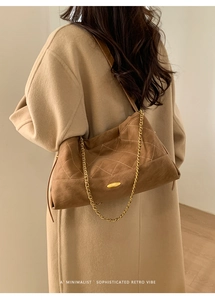 Close-up of brown suede-like quilted bag with golden chain strap on beige coat