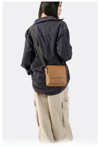 Model wearing a brown leather square crossbody bag with adjustable textile strap