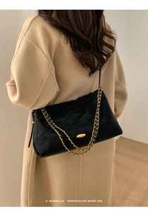 Detail of black suede tote bag with quilted pattern and gold chain strap on model
