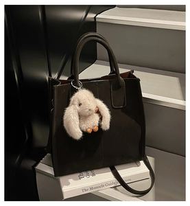 Detail of dark brown tote bag with plush bunny charm on white book background