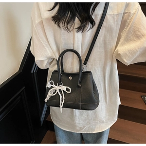 Detailed back view of model wearing a black litchi leather bag with lace bow