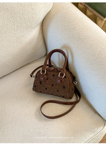 Detail of a brown tweed mini Boston bag with bow prints and leather straps on a sofa