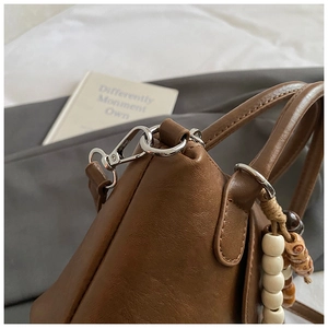 Détail d'un sac à main en cuir marron avec garniture métallique argentée et charm en perles
