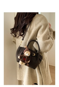 Brown leather crossbody bag with teddy bear charm shown on an oatmeal wool coat