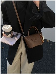 Détail d'un sac bandoulière vintage en cuir marron foncé avec charme en perles de bois
