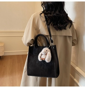 Close-up of black tote bag with plush rabbit pendant worn over the shoulder by a model