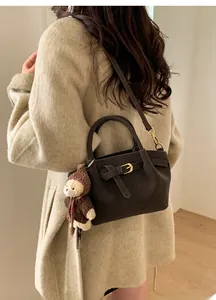 Detail of a dark brown leather bag with golden buckle and cute bear charm on a model