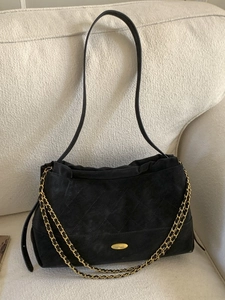 Black quilted suede tote bag with golden chain straps and metal logo on beige sofa