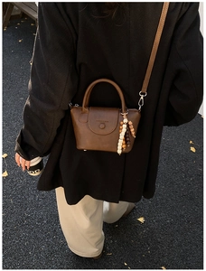 Gros plan d'un sac bandoulière marron rétro sur un blazer noir avec perles