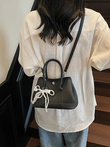 Black pebbled leather tote bag with canvas trim, white lace bow, and pearl decoration