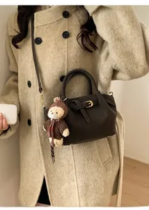 Detail of dark brown suede bucket bag with gold buckle and cute plush bear charm accessory