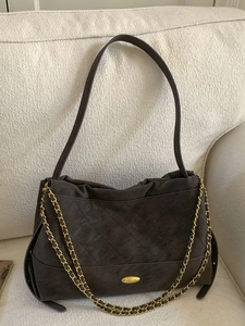 Quilted faux suede tote bag with golden chain straps in dark brown on a beige sofa