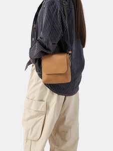 Brown leather crossbody bag with green strap and flap closure in a stylish side view