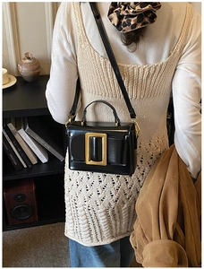Detail of a chic black glossy leather square bag with large gold buckle on a model