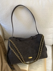 Quilted tote bag in dark brown suede with metal chain strap on a cozy white sofa