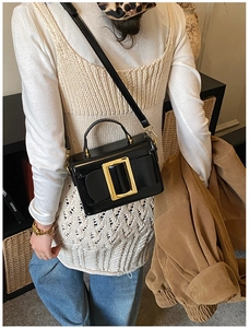 Detail of a chic black square bag featuring a large gold buckle and slim shoulder strap