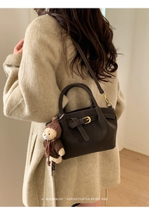 Detail of dark brown leather handbag with gold buckle and cute bear charm accessory