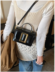 Detail of minimalist black crossbody bag with gold rectangular buckle on beige knitwear