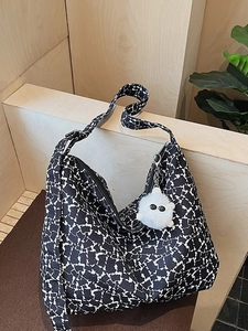 Canvas hobo bag with black and white cow print, wide strap, and plush monster charm