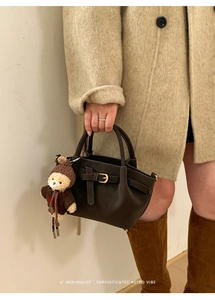 Detail of dark brown leather handbag with buckle decor and cute plush bear charm