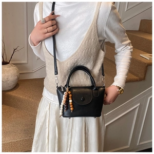 Détail d'un sac à main noir en cuir avec charme perlé et bandoulière amovible