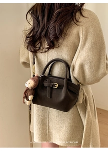 Detail of a dark coffee retro handbag with a small knit bear charm on a beige coat
