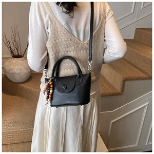 Détail du sac bandoulière noir avec breloque vintage en perles de bois et boucles argent